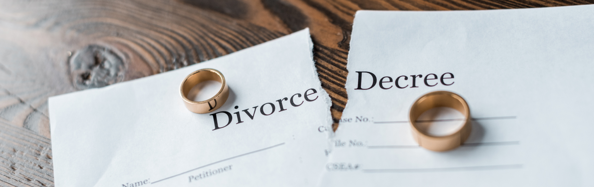 close up shot of teared divorce decree and engagement rings on wooden surface